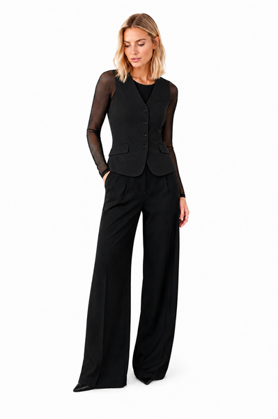 Model wearing the black mesh sleeve layering top under a tailored black vest and wide-leg trousers, demonstrating the sheer mesh sleeves and streamlined silhouette.