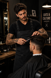 Male barber wearing a black V-neck T-shirt while cutting a client's hair in a modern barbershop, demonstrating professional salon workwear.