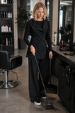 Hairdresser wearing MANHATTAN TUNIC BLACK while sweeping hair in a professional salon